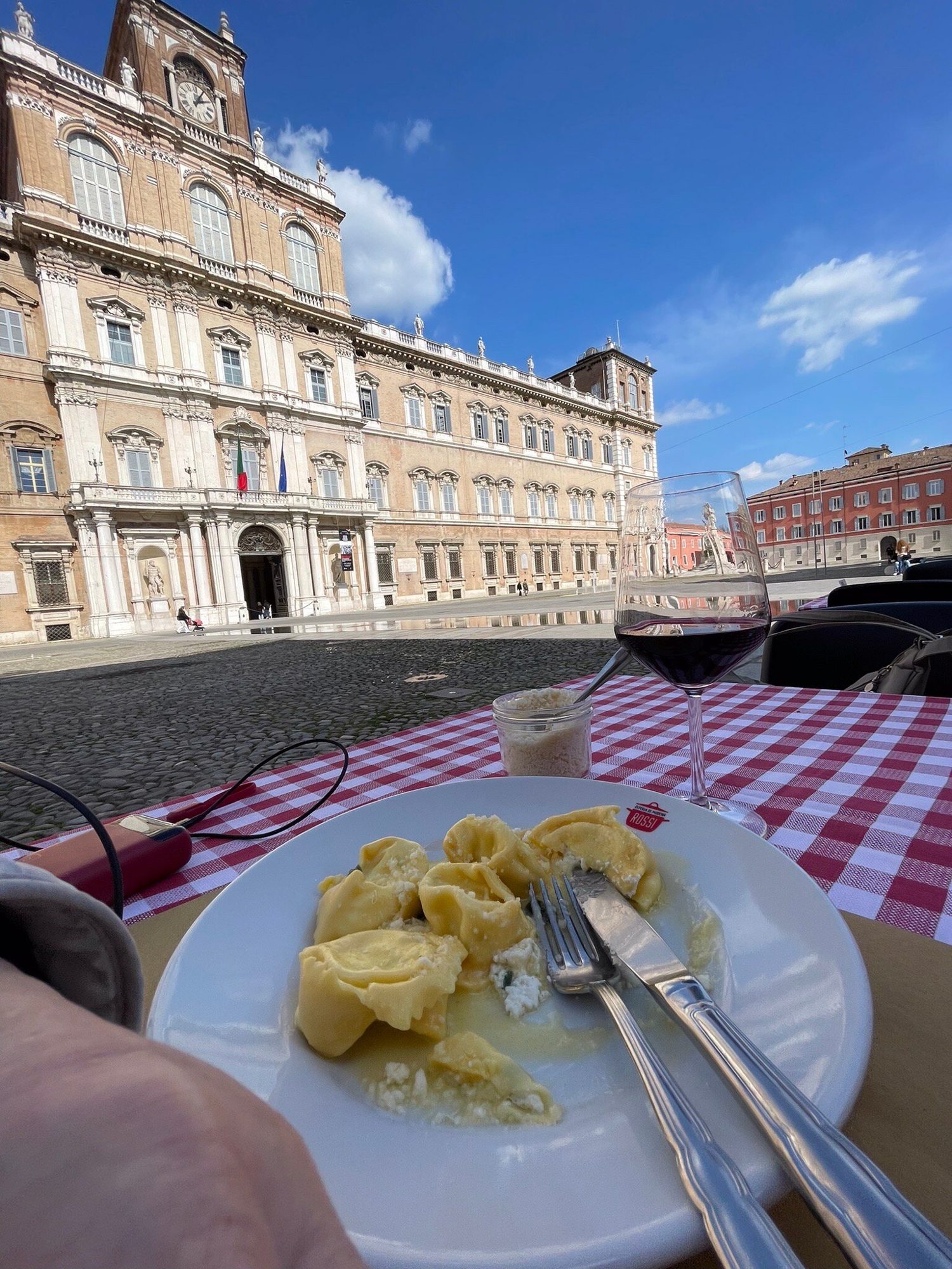 Un piatto di tortellini in primo piano e il Palazzo Ducale di Modena sullo sfondo, dai tavoli in Piazza Roma