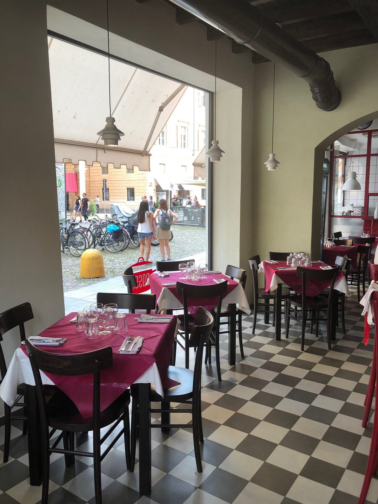 La sala dell'osteria con il pavimento a scacchi bianco e nero e le tovaglie rosse, aperta sul portico di Piazza Roma