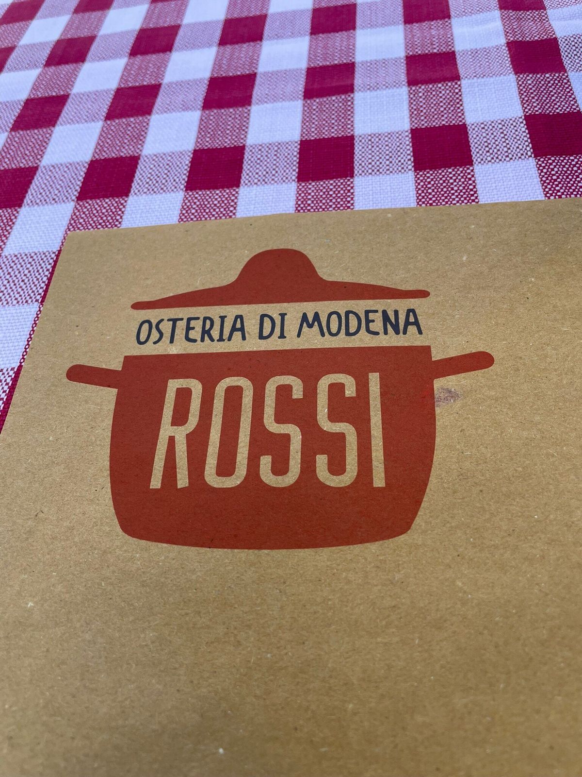 Il marchio dell'Osteria di Modena Rossi, una pentola rossa, stampato sulla tovaglietta di carta